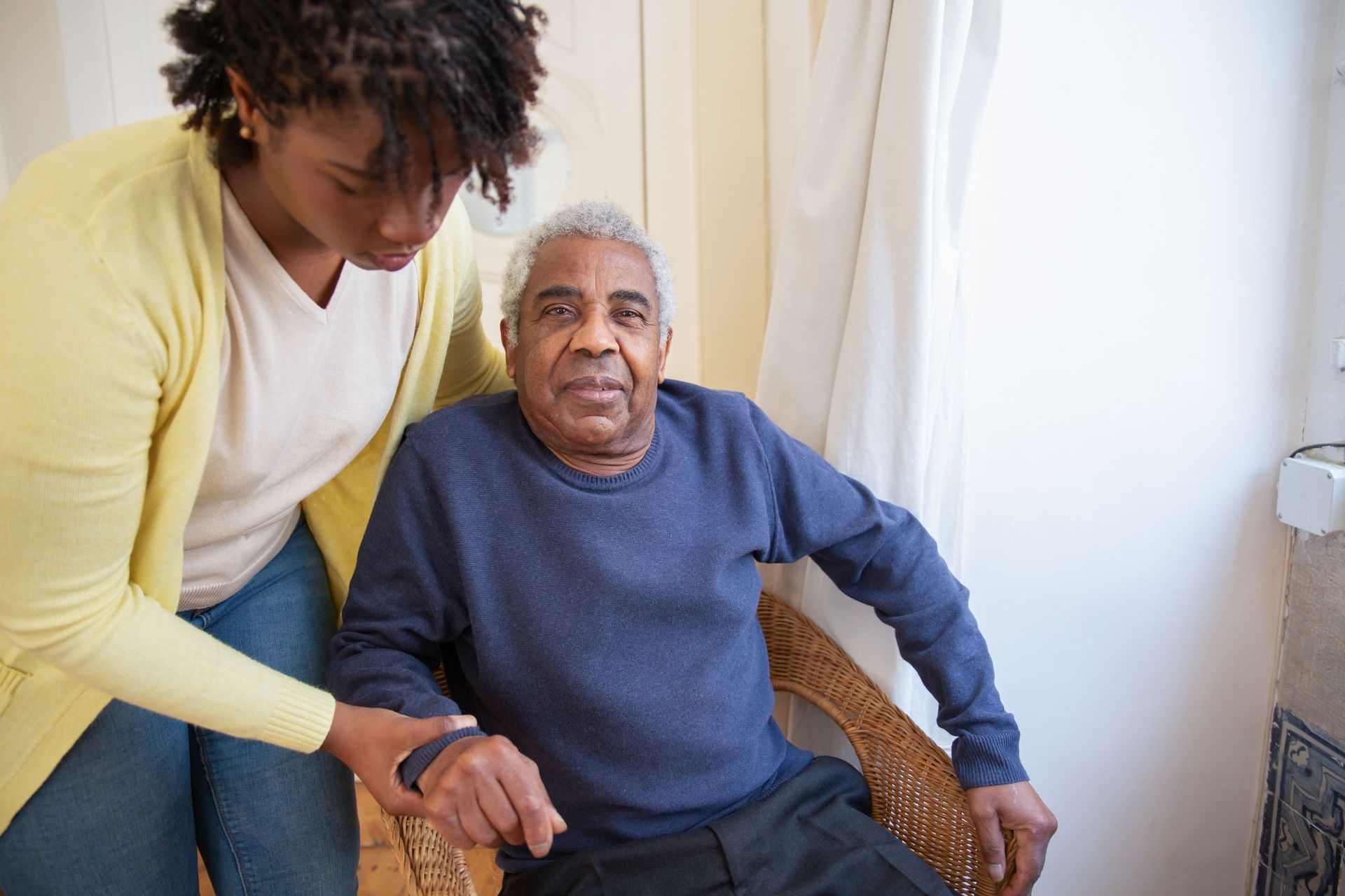 A carer with her arm around an older man sitting in his armchair