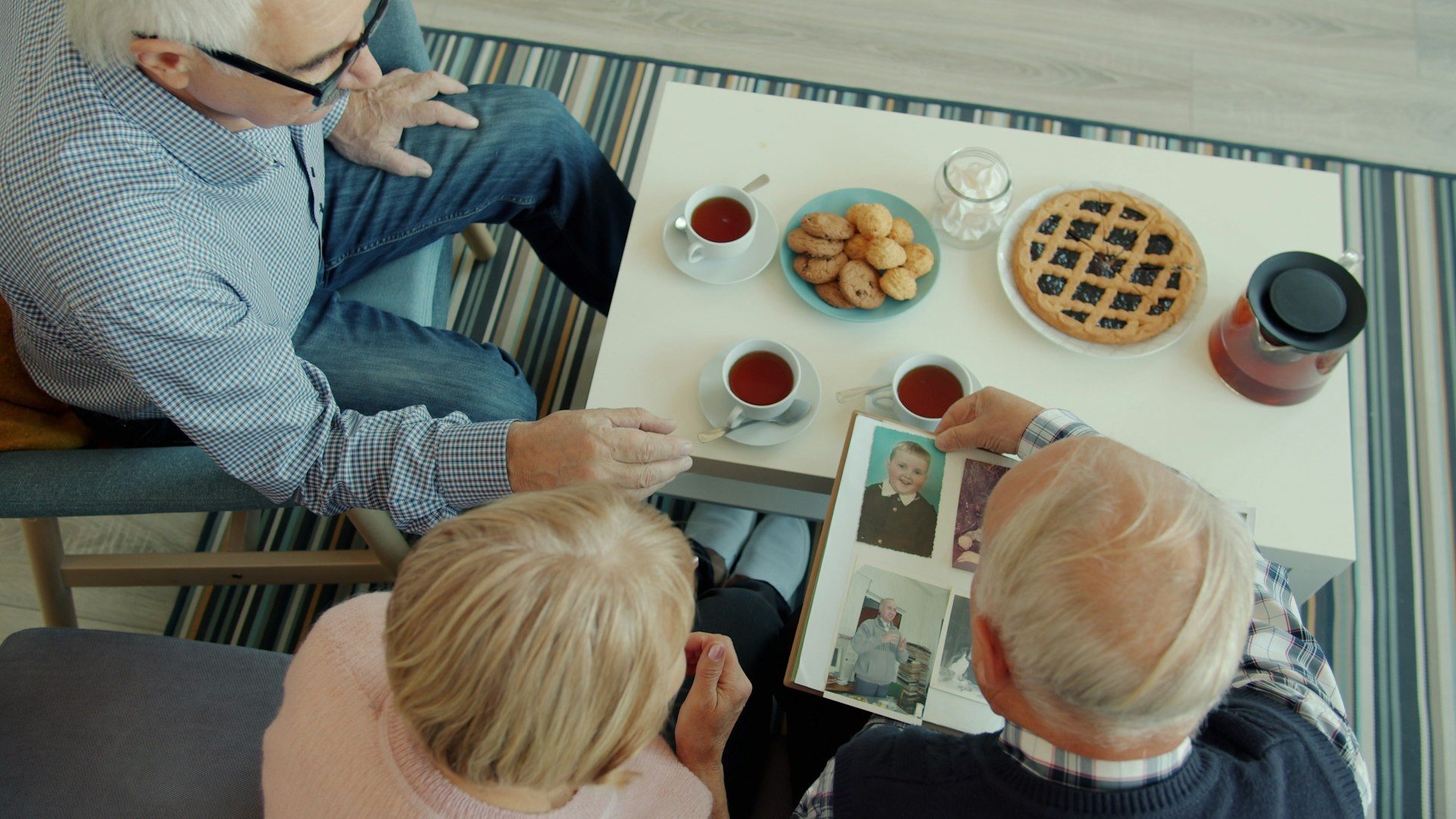 Seniors looking at a photo album with tea and snacks.