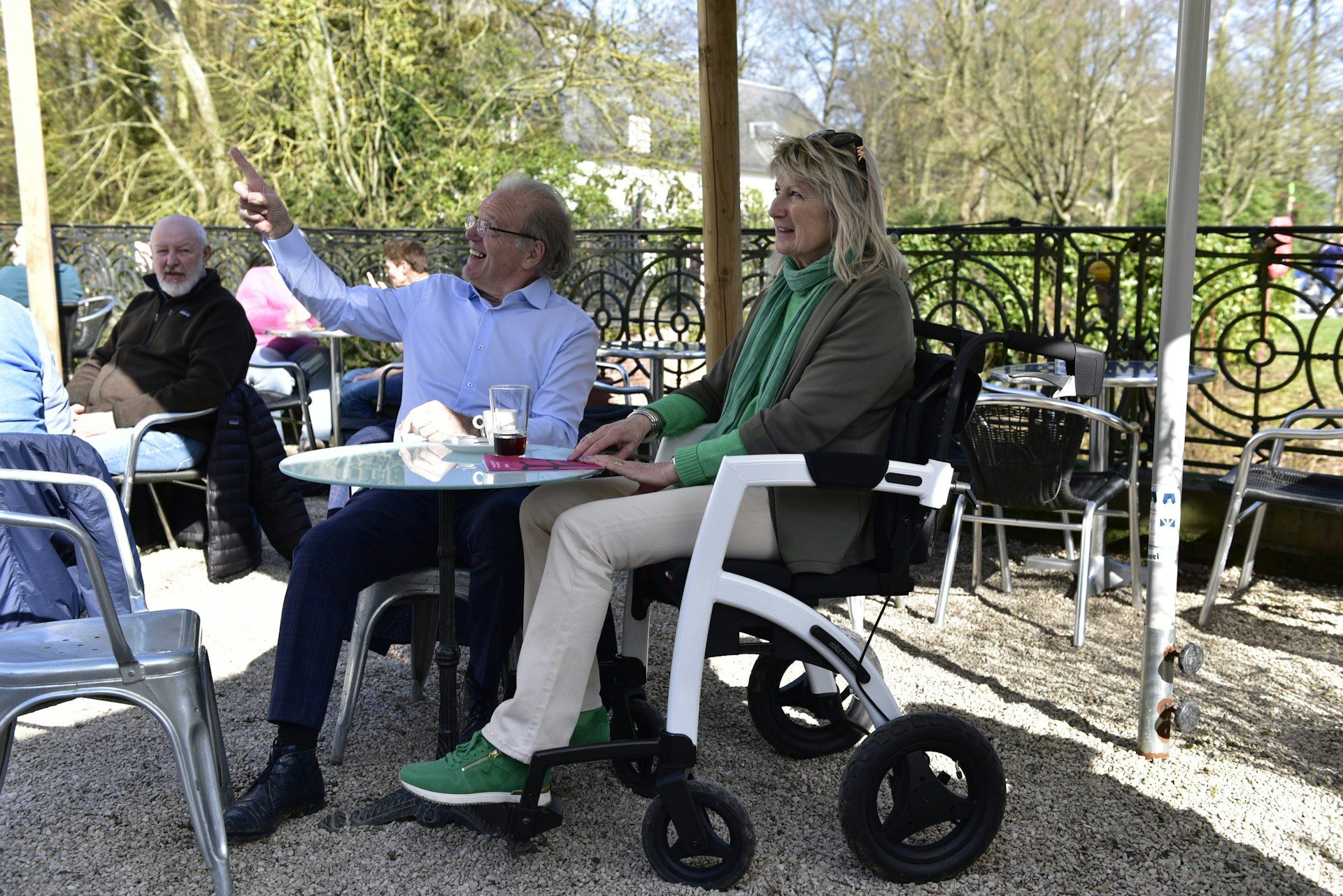 Couple sitting at an outdoor cafe with a wheelchair.